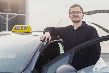 Portrait of smiling caucasian taxi driver near car, looking at camera.の写真素材
