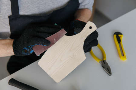 Carpenter hands polishing wooden cutting board with sandpaper close up. Concept of DIY woodwork.の写真素材