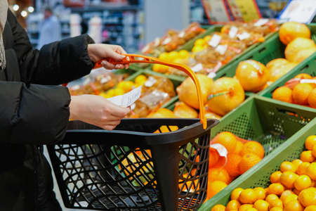Close up of woman at supermarket holding a shopping basket and paper shopping list.の写真素材