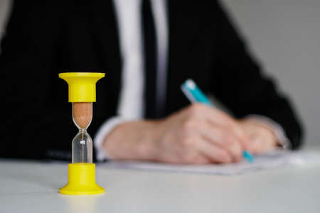 Close-up Of Hourglass In Front Of Businessman Working With Documents In Office.の写真素材