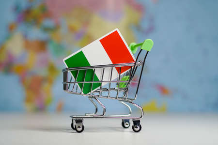 Italian national flag in miniature shopping trolley cart. Shopping online or shipping, duty concept. World map on the background.の写真素材