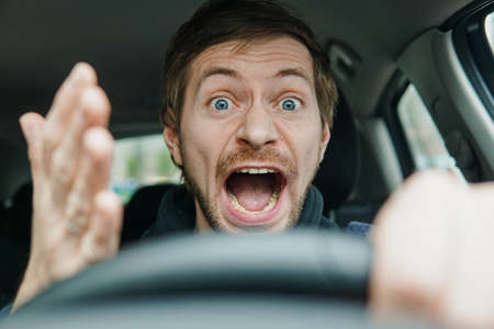 Angry man driving a car. Male driver gesturing and shouting behind the wheel of the car.