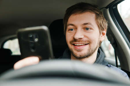 Young smiling male driver using smartphone behind the wheel of the car. Gps, navigation concept.