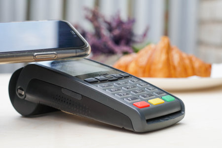 Close up of young woman pays the purchase through the smartphone at bakery. Bank payment terminal. NFC technology.の写真素材