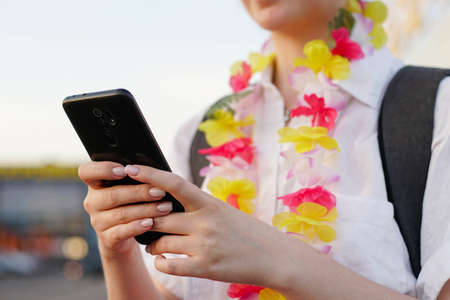Young happy tourist woman in hawaiian necklace using smartphone in airport. Female traveler booking a hotel.の写真素材
