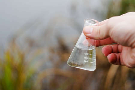 Inspector holding a chemical flask with river water. Water testing for infections.の写真素材