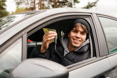 Young smiling man student holding key of new car. Rent car or buying first car concept.の写真素材