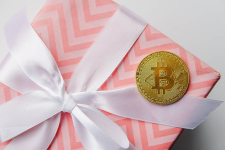 Golden bitcoin on the pink gift box ribbon. Cryptocurrency concept.