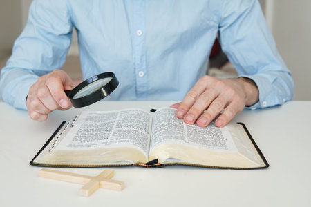 Christian catholic man with magnifying glass searching for answers in old Holy Bible. Loupe on a Bible.の写真素材