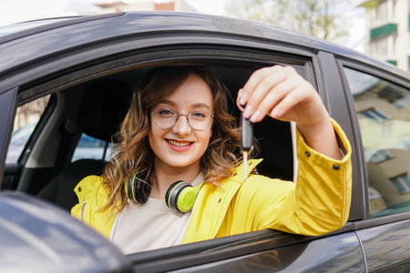 Young smiling girl student holding key of new car. Rent car or buying first car conceptの写真素材