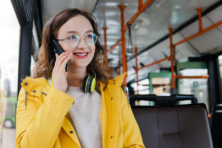 Portrait of smiling young woman commuting by bus talking on phone. Cute charming female student speaking sitting on seat of empty city bus. Public transport concept.の写真素材