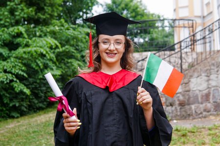 Young italian woman wearing graduation gown and hat holding flag of Italy smiling happy and positive.の写真素材