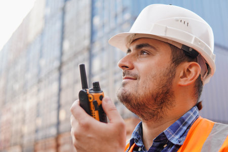 Smiling container worker or engineer talking radio phone or walkie-talkie in container warehouse. Close up.の写真素材