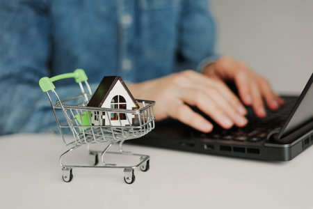 Young man using laptop. Wooden house on the table. Online shopping or payment housing monthly installments credit.の写真素材