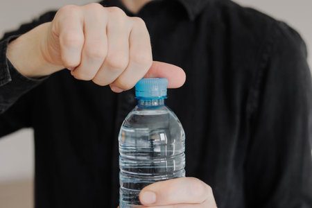 Close-up of man opening the plastic cap of water bottle. Daily water intake.の写真素材