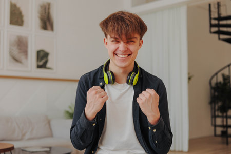 Young excited man in headphones celebrating victory and success with raised arms.の写真素材