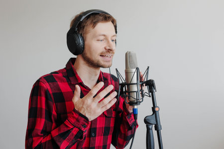 Young man narrator recording audiobook using microphone at recording studio.の写真素材