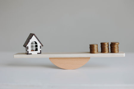 Wooden house and money coins stack on wood scale. Real estate conceptの写真素材