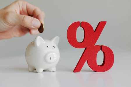 Hand putting coin into piggy bank next to red percent sign. Saving money, bank deposit concept.の写真素材
