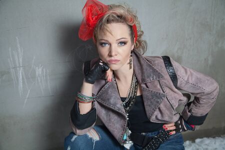Beautiful blonde woman in rock style sits at concrete wall and looking at the cameraの写真素材