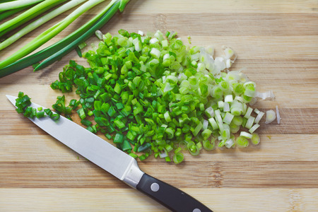 Handful of finely chopped green onions on striped wooden boardの写真素材