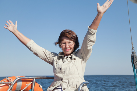 Elderly woman yachtsman on a sailing yacht shows delight at sunny dayの写真素材