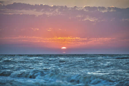 Summer sun rises through the clouds on the sea horizonの写真素材