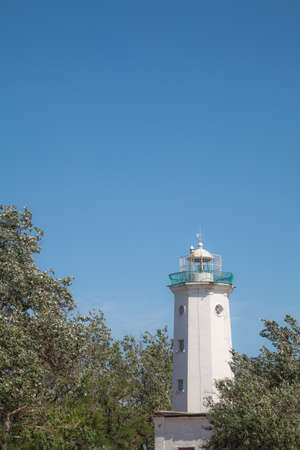Old tower lighthouse against the blue sky and green treesの写真素材
