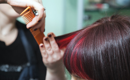 Hands of the hairdresser in motion during women's hairstyles with red hair strandsの写真素材