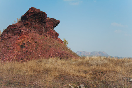 Unusual shape slag heap in meadow with dry grass on background of blue sky and other waste dumpsの写真素材