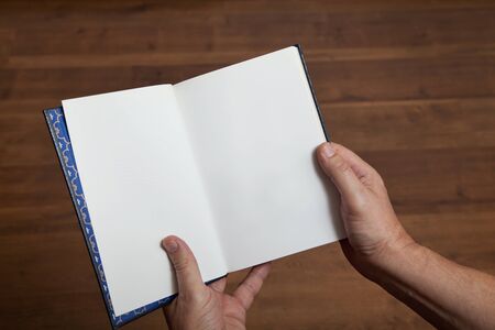Male hands holding an open book on a background of the wooden floorの写真素材