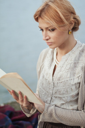 Portrait of beautiful girl in vintage style with a book on autumn nature backgroundの写真素材
