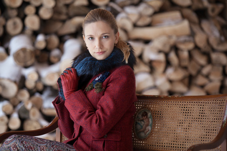 Gentlewoman sitting on a bench in winter veranda on firewood backgroundの写真素材