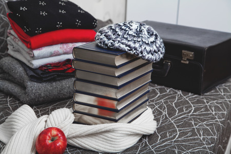 Composition of reading and relaxation at winter trip. Stack of winter clothes with red apple and books with silver edge. Books wrapped beret and warm scarf.の写真素材