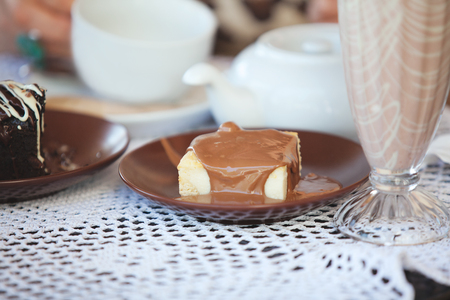 Piece of cake drizzled with milk chocolate on brown plate at table in cafeの写真素材