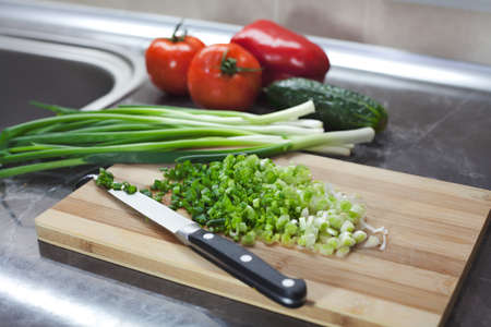 Handful of finely chopped green onions and other vegetables on striped wooden board