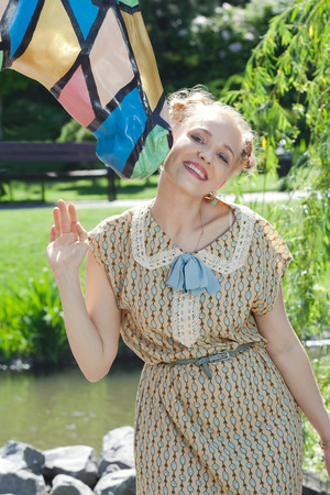 Beautiful romantic blonde girl in retro style standing near statue of horse in summer garden on sunny afternoonの写真素材