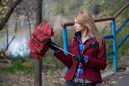 Beautiful blonde in red gloves and short jacket opens checkered umbrellaの写真素材