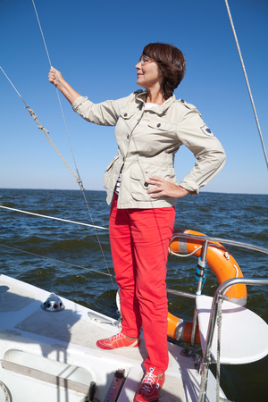 Elderly woman yachtsman on a sailing yacht holds on to the ropes at sunny dayの写真素材