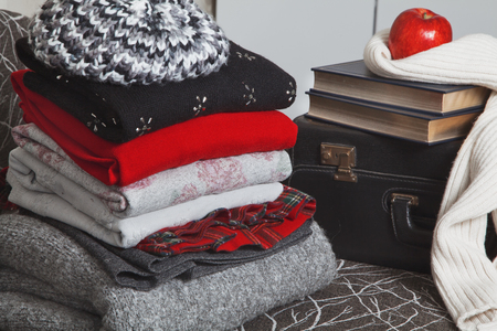 Composition of reading and relaxation at winter trip. Stack of winter clothes with red apple and books with silver edge. Books wrapped warm scarf.の写真素材