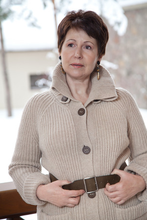 Attractive elderly woman in knitted coat posing on outdoor terrace at winter dayの写真素材