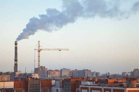 Boiler pipe smoke above roofs of high-rise apartment buildings at sunsetの写真素材