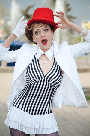 Circus artist woman in red hat posing outdoors with a surprised expression on her faceの写真素材