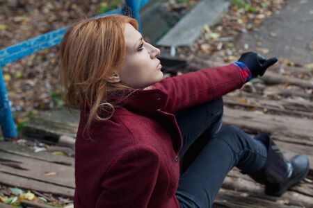 Pretty woman with flowing hair in tweed jacket and leather gloves sits on the old bridge in autumn forestの写真素材