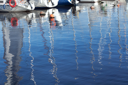 Reflection of masts in the blue water near the pier for sailing yachtsの写真素材