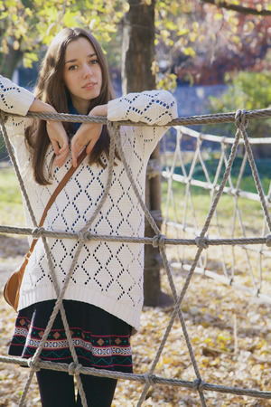 Beautiful young teenage girl posing near a rope fence at bright sunny autumn dayの写真素材