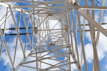 Bottom view power transmission high voltage lines on the white supports against blue skyの写真素材