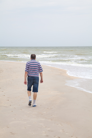 Man in shorts walking on sea beach in overcast dayの写真素材