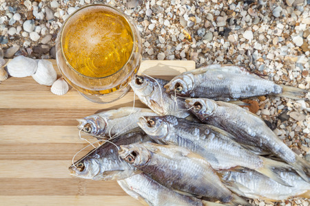 Bunch of dried fish on a wooden board next to a glass of beerの写真素材