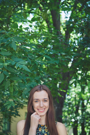 Young beautiful brown-haired teen girl with long hair smiling at the camera in a summer parkの写真素材